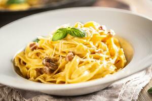 Italienisch Essen Pasta Tagliatelle Carbonara mit Speck Parmesan Ei Eigelb und Basilikum Blätter foto