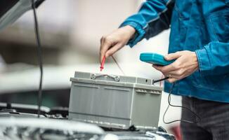 Auto zurückgezahlt Garage Techniker prüft Lebensdauer von ein Auto Batterie mit ein Multimeter foto