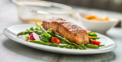 geröstet Lachs Steak mit Spargel Brokkoli Karotte Tomaten Rettich Grün Bohnen und Erbsen. Fisch Mahlzeit mit frisch Gemüse foto