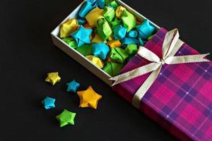 farbige Geschenkbox mit Satinschleife mit Origami-Papiersternen auf schwarzem Hintergrund