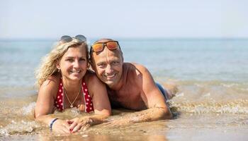 ein Mitte alt Paar Lügen auf ein Strand durch das Meer während ein heiß Sommer- Tag Ausgaben ein Ferien zusammen foto