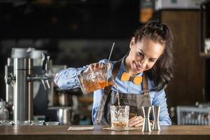 gut aussehend Kellnerin gießt alt gestaltet Cocktail in ein Zier Glas im ein Kneipe foto