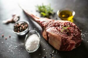 roh Tomahawk Steak mit Salz- Gewürze Knoblauch und Kräuter auf ein alt rustikal Tafel foto