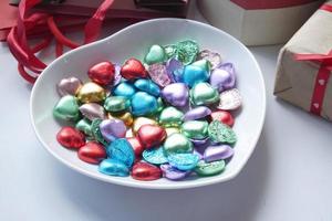 kleines herzförmiges Geschenk mit Süßigkeiten im Teller auf weiß foto