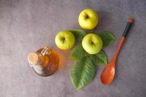 Apfelessig in einer Flasche und grüne Äpfel auf dem Tisch foto