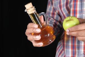 Hand hält Apfelessig in Glasflasche mit frischem grünem Apfel