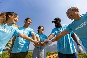 Mannschaft von jung und Vielfalt Freiwillige Arbeiter Gruppe genießen wohltätig Sozial Arbeit draussen zusammen im Speichern Umgebung Projekt tragen Blau T-Shirt während Beitritt Hand im Leistung montieren Einheit foto