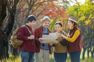glücklich asiatisch Familie mit Senior Elternteil sind Gehen zusammen im Öffentlichkeit Park während Herbst mit Ahorn und Ginkgo Baum während suchen beim Karte zum fallen Farbe Reise Ziel und Familie glücklich Ferien foto