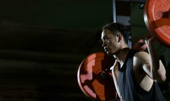 asiatisch muskulös Sport Mann ist trainieren Gewicht Ausbildung auf Kreuzheben Hantel zum Ader Muskel Innerhalb Fitnessstudio mit dunkel Hintergrund zum ausüben und trainieren Konzept foto
