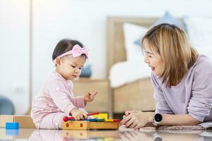 asiatisch Mutter ist spielen mit ihr ziemlich lächelnd Baby Tochter mit hölzern Spielzeug Block während Ausgaben Qualität Zeit im das Bett zum Familie Glück und Erziehung Konzept foto