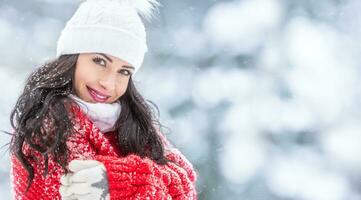 glücklich Frau ruht ihr Waffen auf das Truhe bedeckt im Schneefall während tragen winter gestrickt Oberbekleidung draußen foto