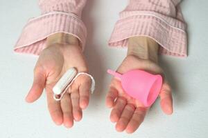 Nahansicht von ein Frau halten ein Wahl von Tampon oder Silikon Menstruation- Tasse im ihr Hände. Alternative ökologisch feminin Hygiene Produkt während Menstruation abfallfrei Konzept foto