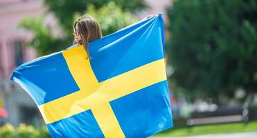 glücklich Mädchen Tourist Gehen im das Straße mit Schweden Flagge foto