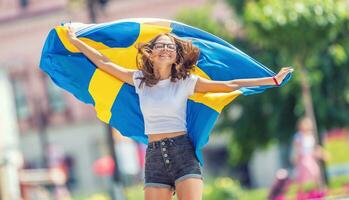 glücklich Mädchen Tourist Gehen im das Straße mit Schweden Flagge foto