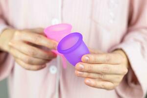 Nahansicht von ein Frau Hände halten ein Silikon Menstruation- Tasse. Alternative ökologisch feminin Hygiene Produkt während Menstruation abfallfrei Konzept foto