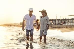 ein mittleren Alters Paar Gehen Hand im Hand auf das Strand beim Sonnenuntergang foto