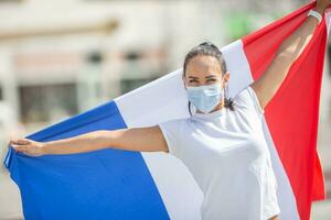 weiblich im ein Gesicht Maske hält ein Französisch Flagge auf das Straße, feiern ein Sieg foto