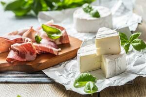 Camembert oder Brie Käse und Schweinefleisch Schinken Prosciutto mit Basilikum Blätter auf Tabelle foto