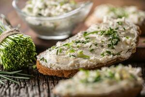 Schnittlauch Sahne Käse Verbreitung auf ein Brot Scheibe Nächster zu Bündel von frisch Schnitt Schnittlauch und ein Schüssel von Verbreitung im das Hintergrund foto