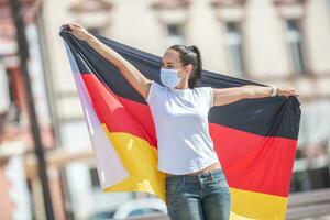 Frau tragen ein Gesicht Maske hält ein Flagge von Deutschland hinter ihr foto