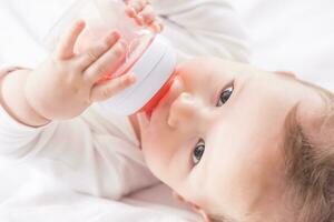Baby Junge Lügen auf Bett und Trinken Tee von ihr Plastik Flasche. foto