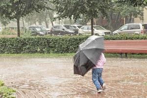 ein kleines Mädchen hat Spaß beim Herumlaufen mit einem Regenschirm bei starkem Regen