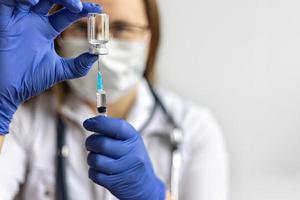Eine Ärztin, die eine medizinische Maske trägt, zieht den Coronavirus-Impfstoff in eine Spritze foto
