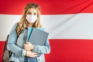 weiblich Schüler im Gesicht Maske steht im Vorderseite von Flagge von Österreich foto