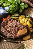 saftig Rindfleisch Rippe Auge Steak geröstet Kartoffeln mit Soße gegrillt Gemüse Salz- Pfeffer und Kräuter im Jahrgang schwenken foto