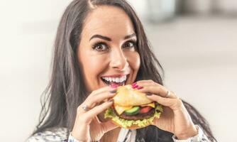 schön Frau halten ein Burger im ihr Hände mit ein Lächeln foto