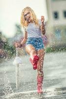 heiter Mädchen Springen mit Weiß Regenschirm im gepunktet rot Galoschen. heiß Sommer- Tag nach das Regen Frau Springen und planschen im Pfütze foto