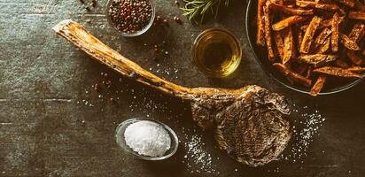 gegrillt Rindfleisch Tomahawk Steak mit Süss Kartoffel Fritten Salz- Gewürze Olive Öl und Rosmarin auf rustikal Tafel - - oben von Aussicht foto