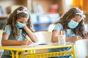 Zwilling Schwestern mit Gesicht Maske zurück beim Schule während covid-19 Quarantäne foto