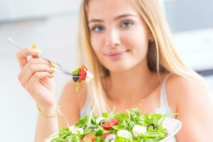 jung glücklich blond Mädchen Essen gesund Salat von Rucola Spinat Tomaten Oliven Zwiebel und Olive Öl foto