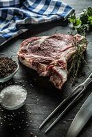 Rippe Auge Steak mit Knochen auf Metzger Tafel mit Kräuter Salz- Pfeffer Gabel und Messer foto