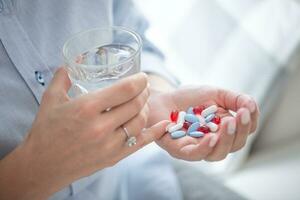 genug Tabletten zu Überdosis ein Person gehaltenen im ein Hand von Frau mit ein Glas von Wasser im das andere Hand foto
