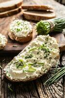 Porträt von Brot Scheibe mit traditionell slowakisch brynza Sahne Käse Verbreitung mit frisch Schnitt Schnittlauch platziert auf rustikal Holz foto