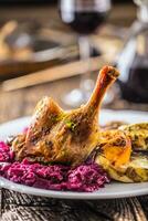 Portion von braten Ente Bein rot Kohl hausgemacht Knödel auf Teller und rot Wein auf das Hintergrund foto