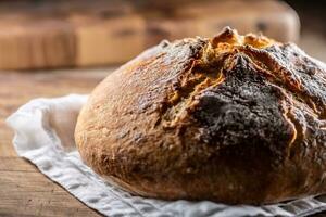 hausgemacht gebacken knusprig Brot setzt auf ein Leinen- Handtuch und hölzern Schneiden Tafel foto