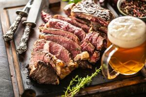 Scheiben von saftig Rindfleisch Steak Gabel Messer Gewürze Salz- Pfeffer Kräuter und Entwurf Bier foto