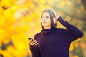 Porträt von glücklich jung Mädchen mit Kopfhörer und Smartphone zuhören Musik- im Herbst Park foto