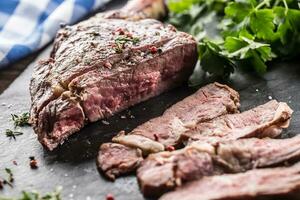 frisch gegrillt Tomahawk Steak auf Schiefer Teller mit Salz- Pfeffer Rosmarin und Petersilie Kräuter. geschnitten Stücke von saftig Rindfleisch Steak foto