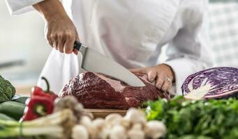 Stück von Schweinefleisch Fleisch Schnitt mit ein Scharf Messer durch Fachmann Koch mit viel von Gemüse um foto
