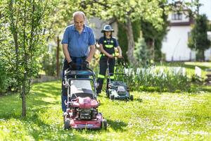 Alten Großvater Lehren ihr Enkelin Wie zu verwenden Mäher und Schnitt Gras. Sie Arbeit im das rustikal Garten im das Dorf foto