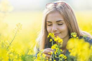 schön jung Mädchen riecht Gelb Blumen auf ein Wiese mit ihr Augen geschlossen, lächelnd foto