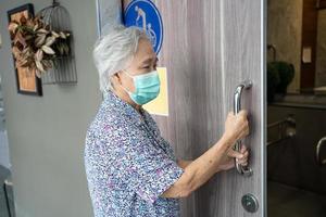 asiatische senior oder ältere alte damenpatientin, die eine gesichtsmaske trägt, öffnet die toilettentür für behinderte menschen zum schutz der sicherheitsinfektion covid-19 coronavirus. foto
