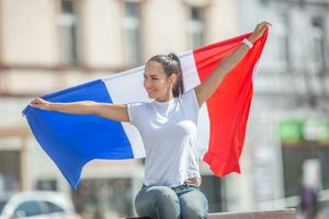 schön Frau sieht aus zu das Seite lächelnd, halten ein Flagge von Frankreich hinter ihr foto