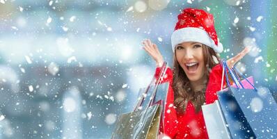 Weihnachten Einkaufen. attraktiv glücklich Mädchen mit Anerkennung Karte und Einkaufen Taschen im Santa Hut. schneebedeckt Atmosphäre. foto