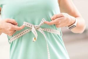 Gewicht Verlust und schlank Körper von ein jung Frau. Mädchen Messung ihr Taille Körper mit messen Band foto