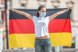 Frau tragen ein Gesicht Maske hält ein Flagge von Deutschland hinter ihr foto